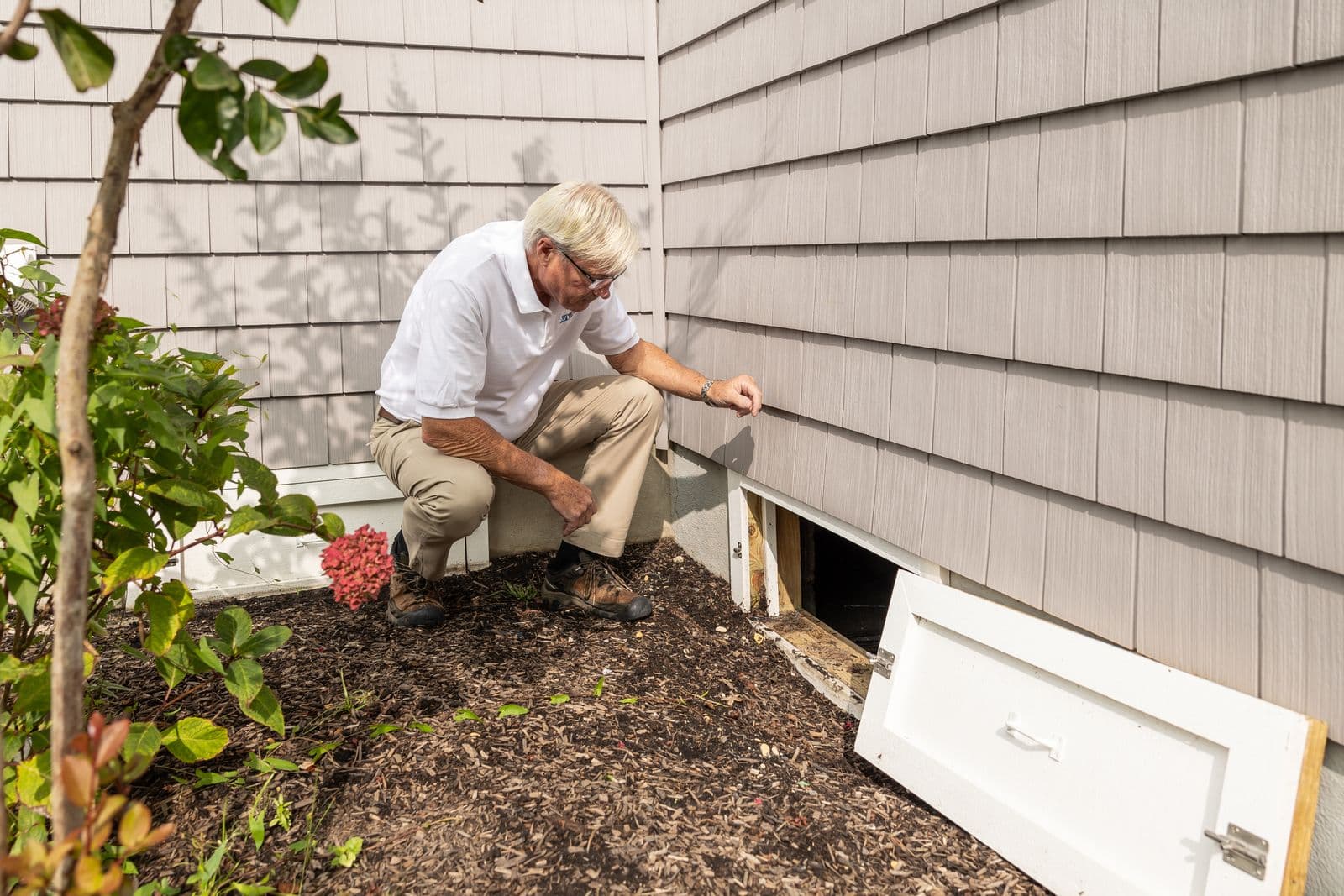 A person inspecting the exterior foundation area of a residential house.